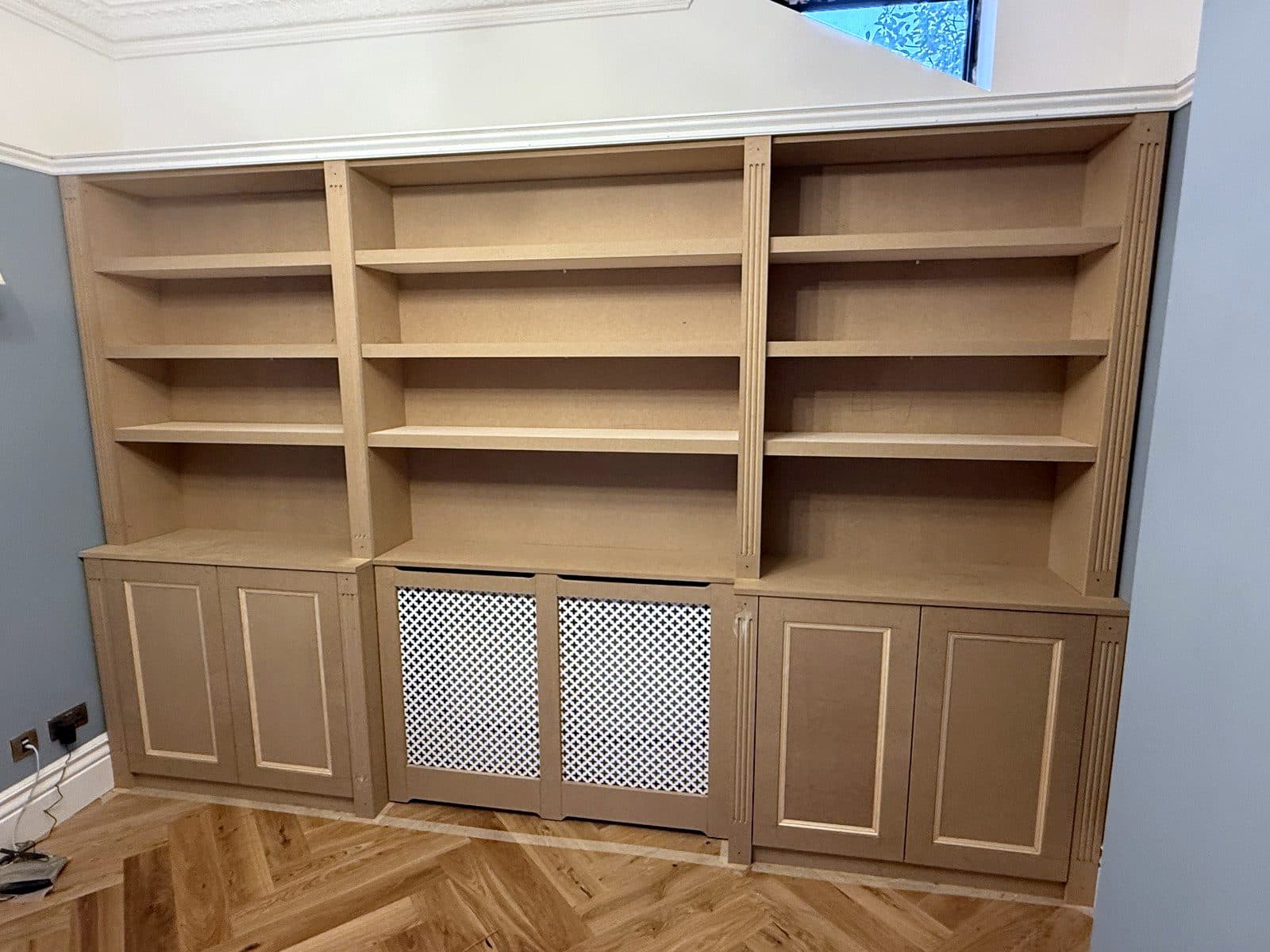 The whole wall: three bays of shelves over cupboards and the radiator cover