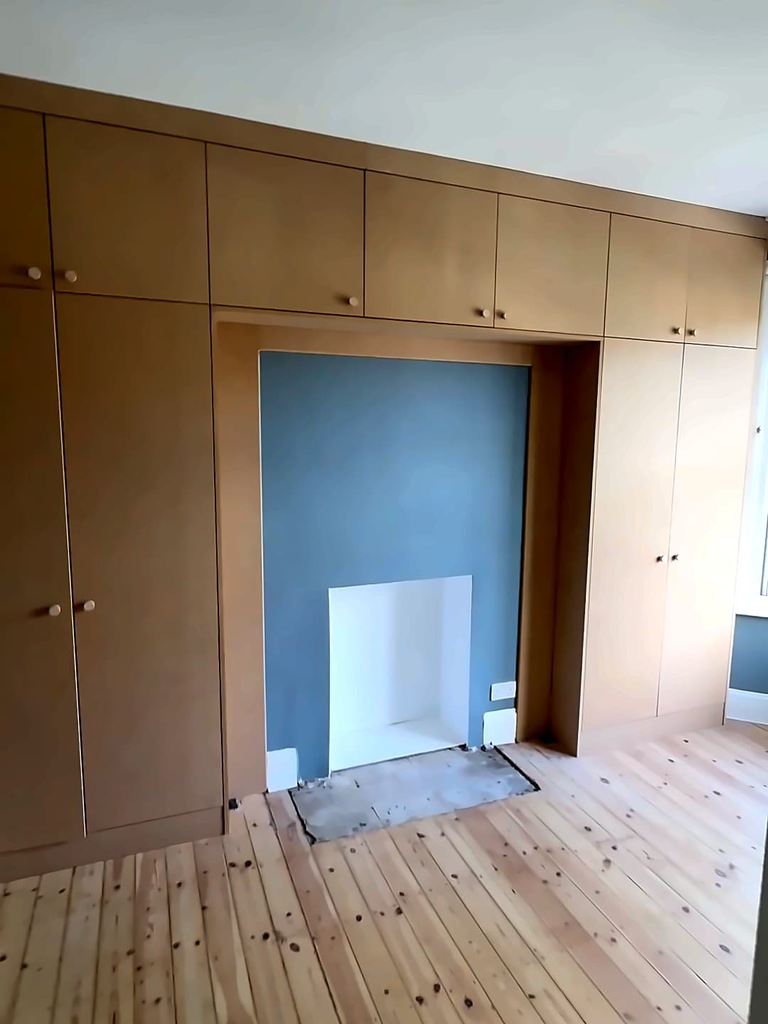Wall of MDF wardrobes built around a chimney breast, with cupboards over the fireplace