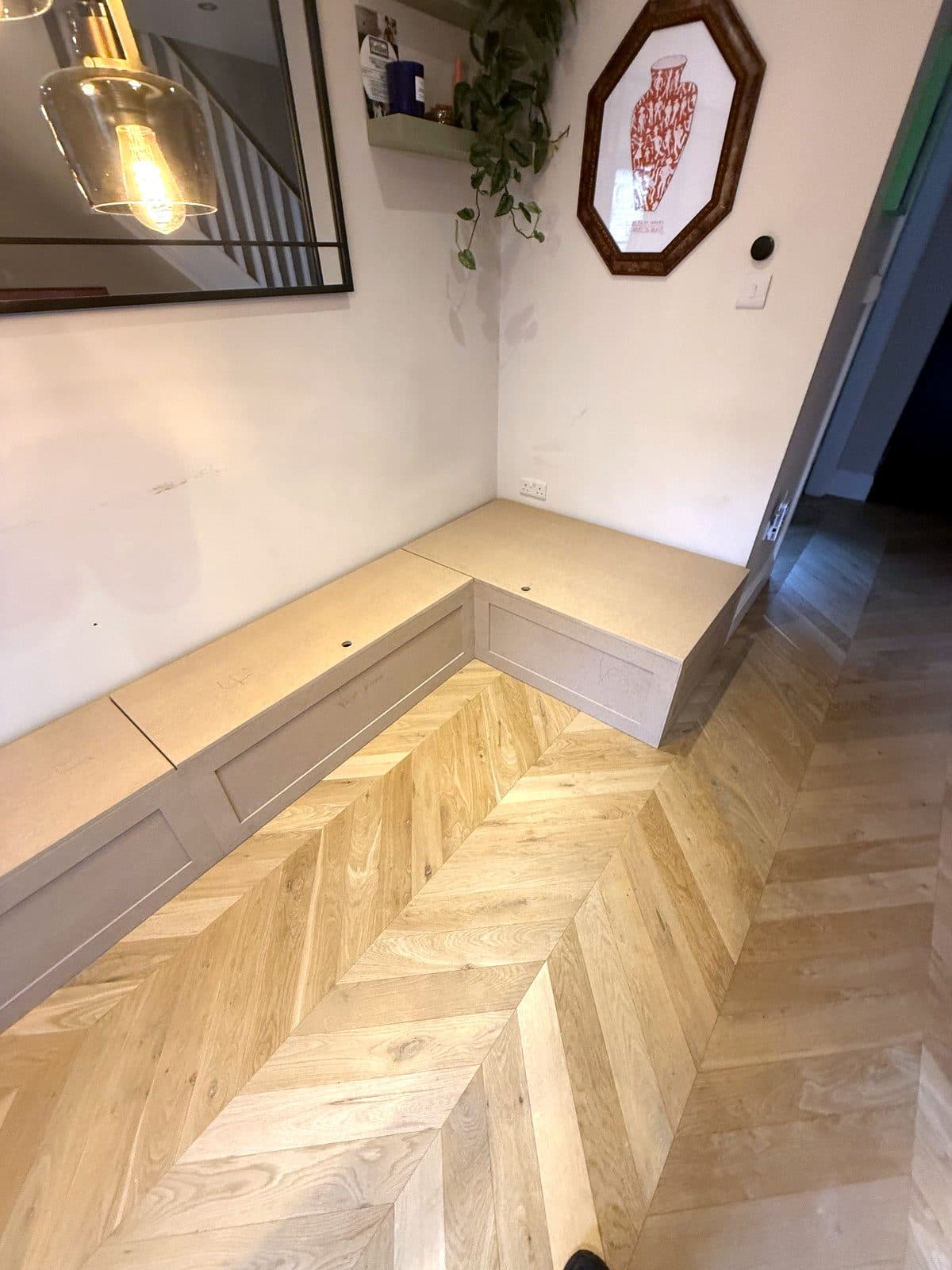 L-shaped MDF storage bench along a wall and round a corner, on a chevron oak floor