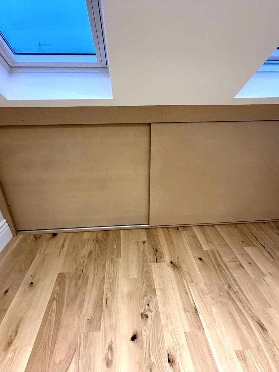 Two MDF sliding doors closed along the low wall of a loft room under two skylights