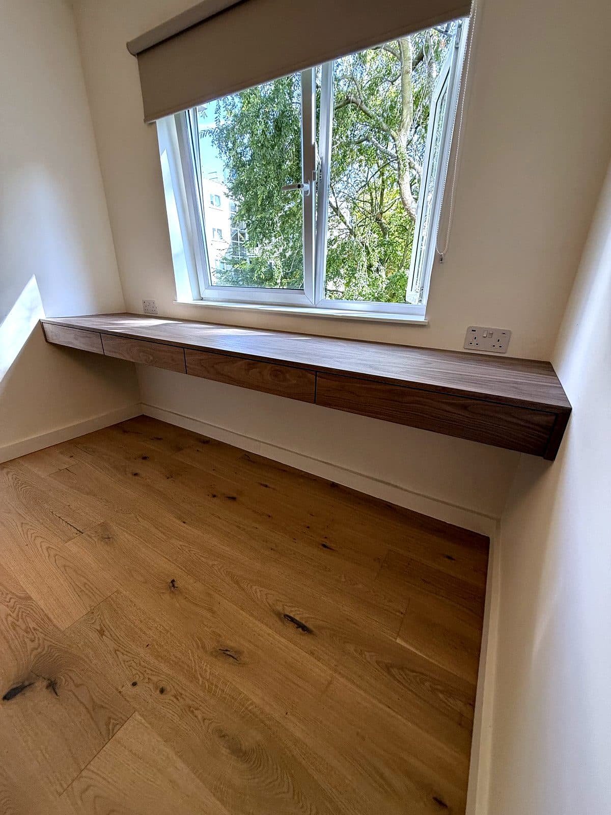 Birch ply room with a tall wardrobe, overhead cupboards and a wall-hung desk lit by a wall lamp