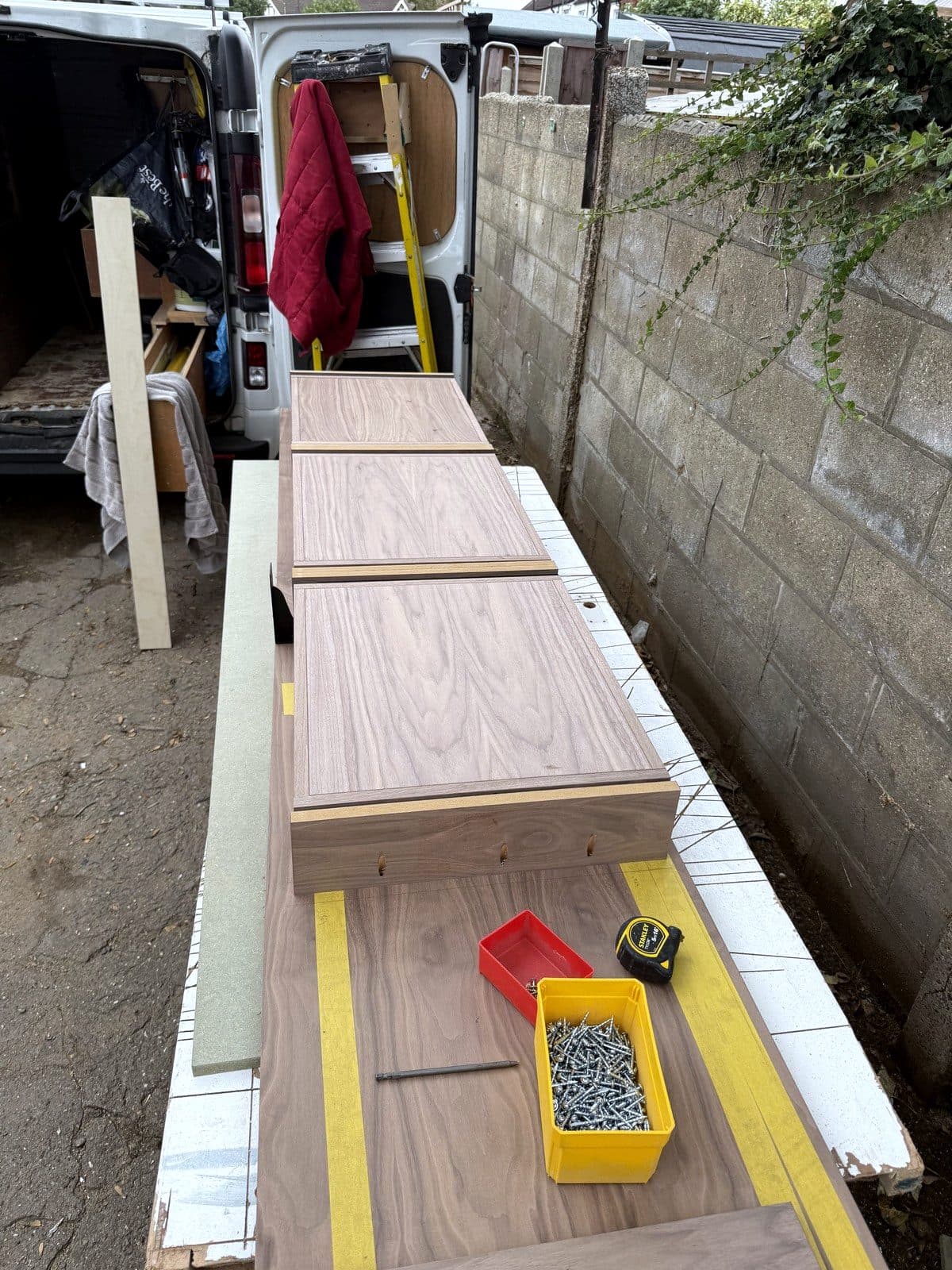 Walnut drawer boxes laid out on trestles outside the van
