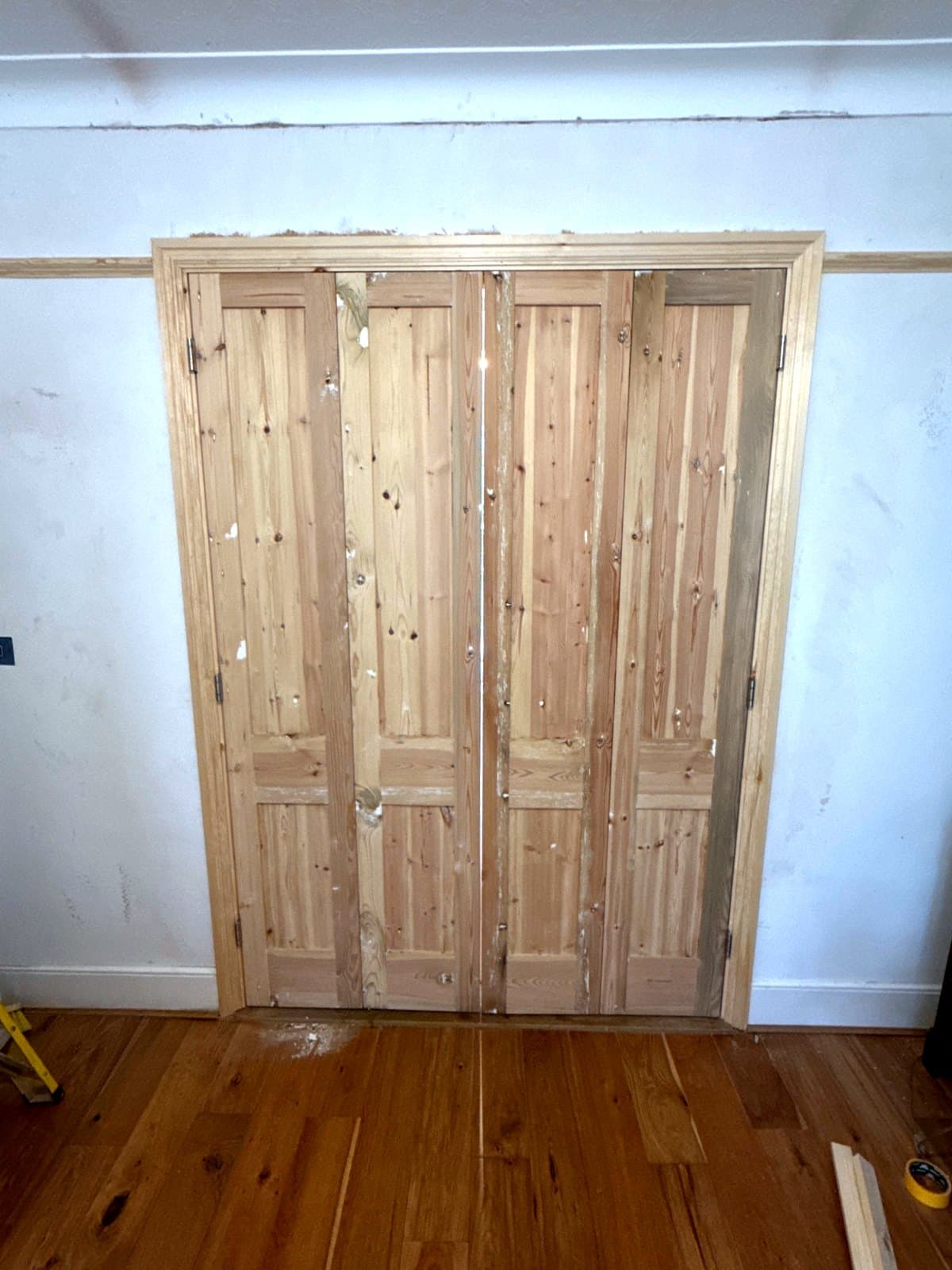 Four pine folding doors closed across a wide opening, with new architraves
