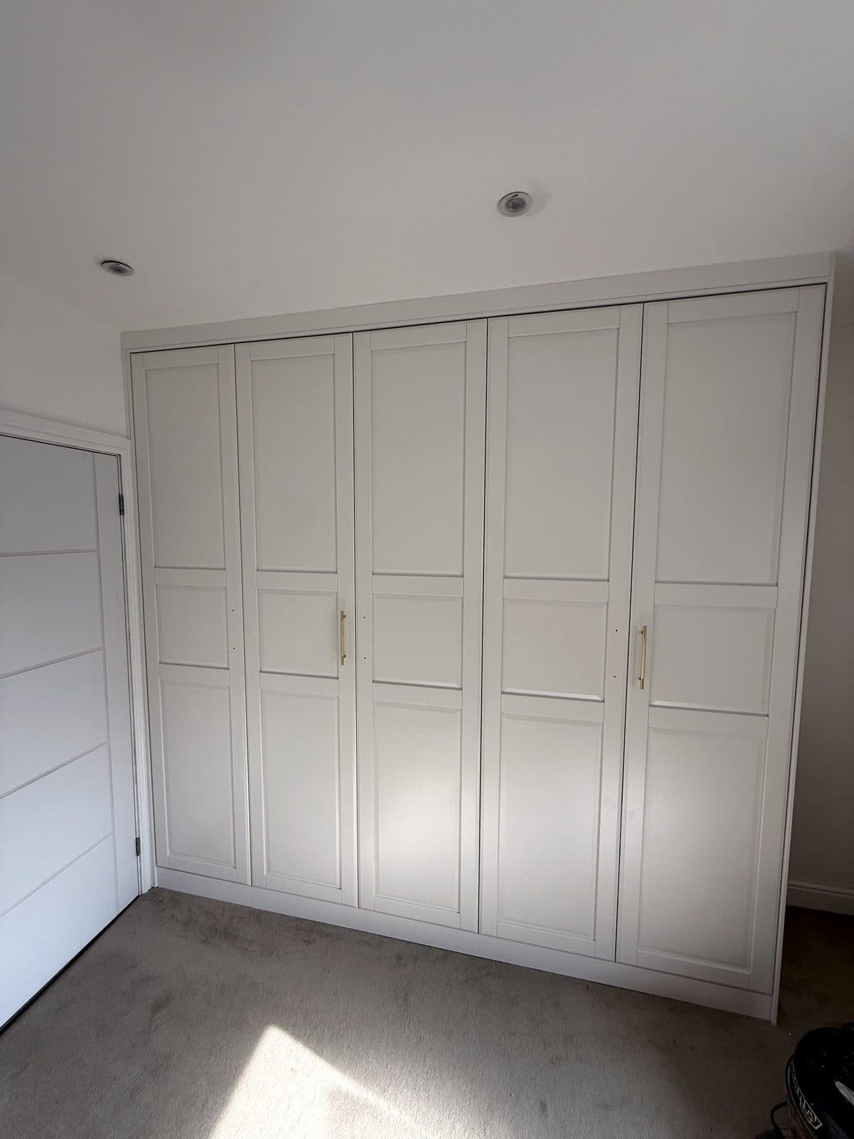 White five-door panelled wardrobe with gold handles, built in to the ceiling