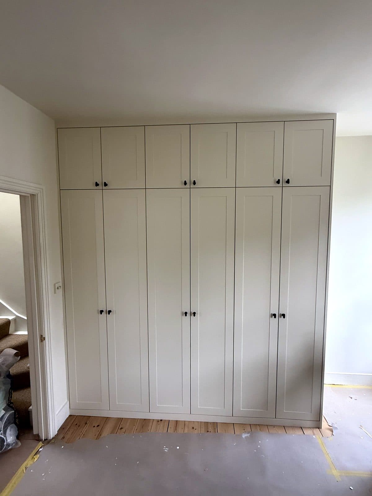 Full wall of wardrobes with painted panelled doors up to the ceiling
