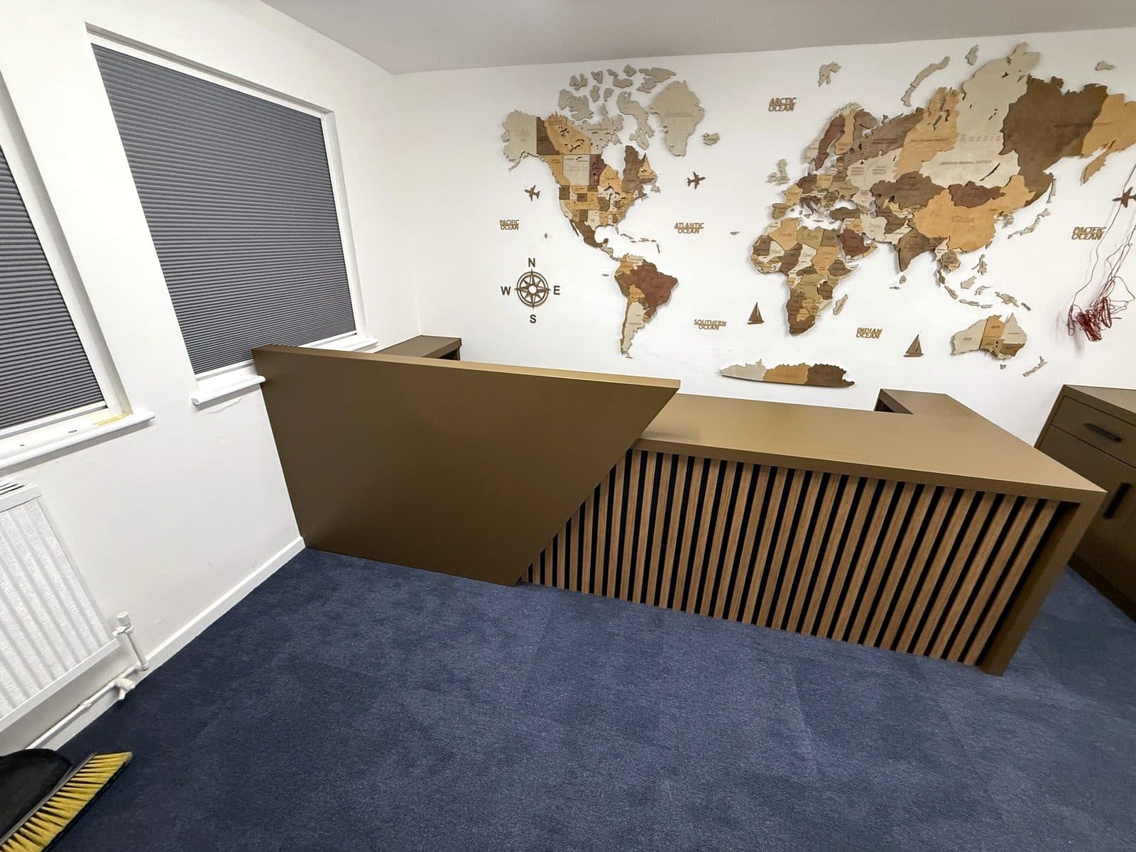 Dark painted L-shaped reception desk with a slatted front in front of a world map wall