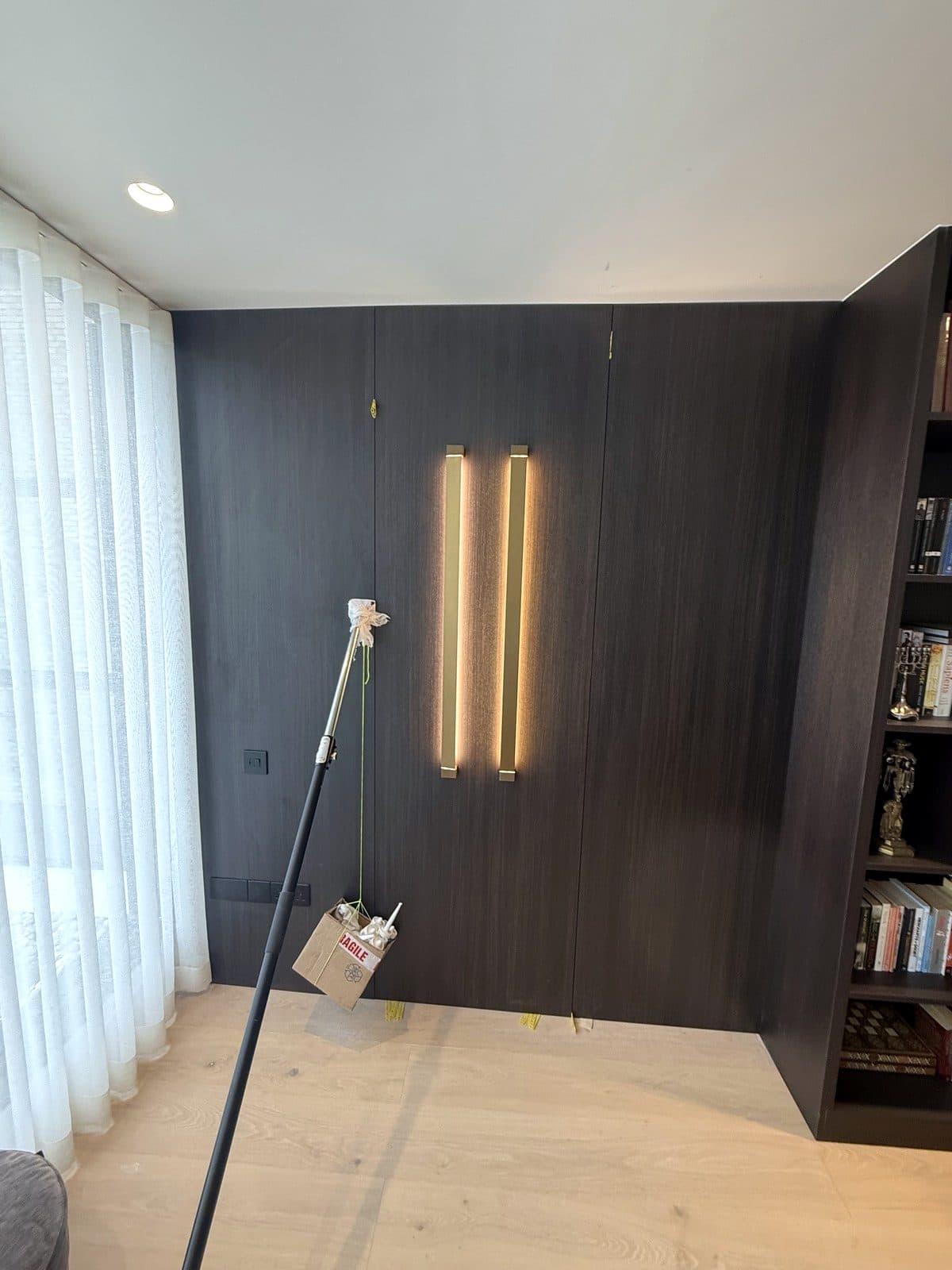 Dark panelled wall with two glowing vertical brass light strips beside a bookcase