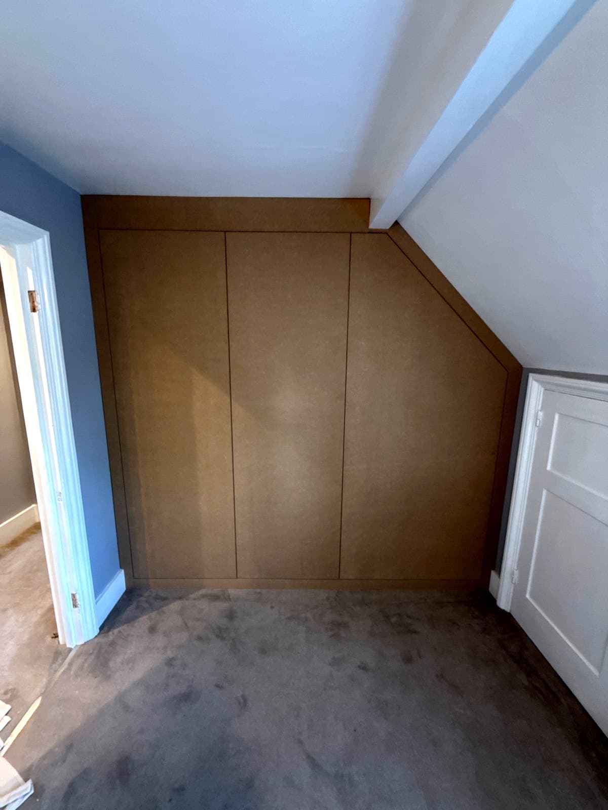 Finished MDF loft wardrobe with three flush doors, the right one cut to the roof slope