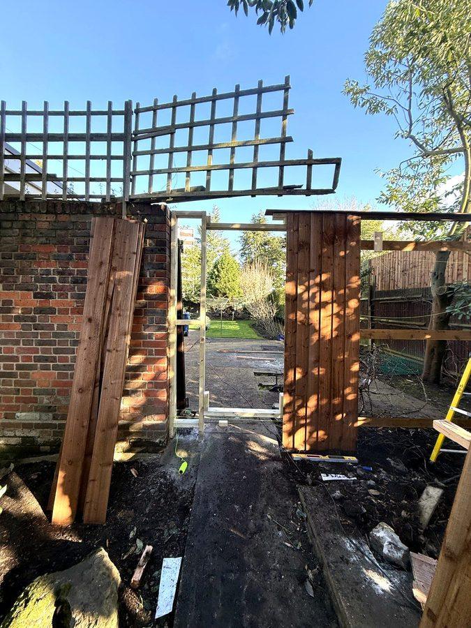 The old trellis above the brick wall, new boards leaning against it